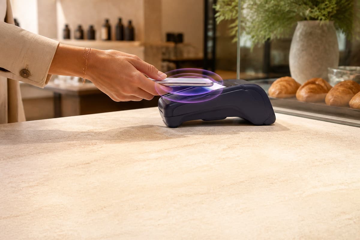 A shopper taps a phone on a merchant terminal as purple reward light begins to form.